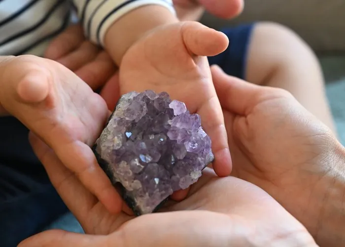 Een kinderhandje en Lindes handen rond een amethist