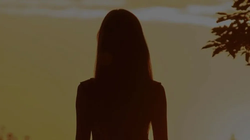 Vrouw die bij zonsondergang buiten wandelt, met de rug naar ons toe