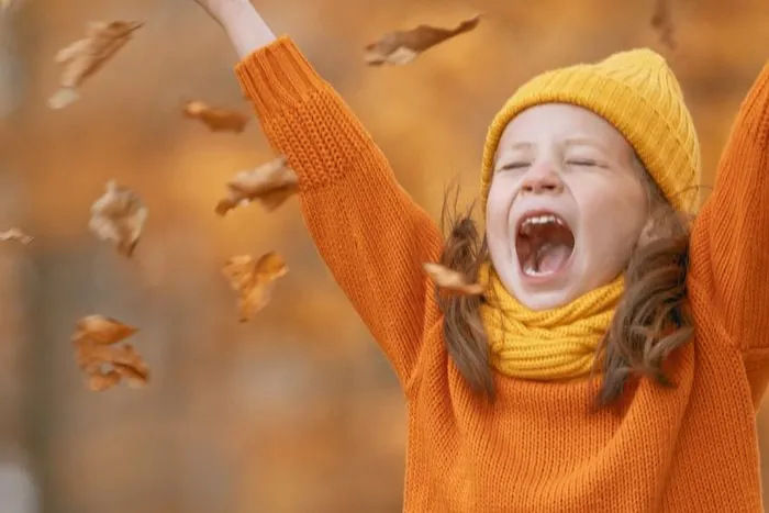 Kind dat juichend herfstbladeren in de lucht gooit