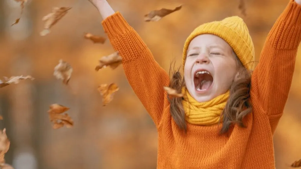 Kind dat juichend herfstbladeren in de lucht gooit