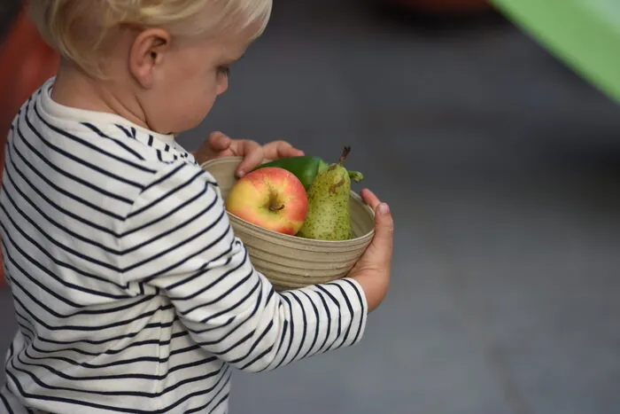 Kind draagt een schaal met geoogst fruit en groenten