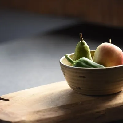 Een houten schaal met peren en een appel in het ochtendlicht
